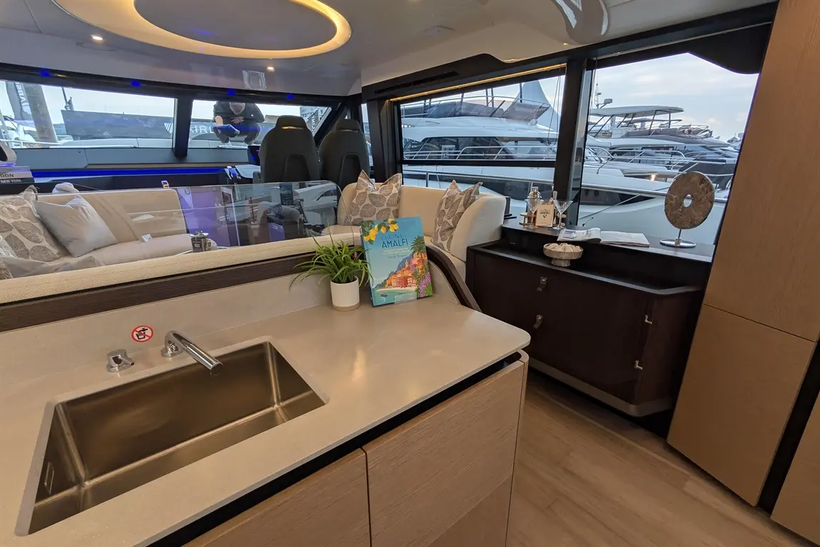 Interior of a luxury yacht showing a kitchen area, seating, decorative items, and views of parked boats through large windows.
